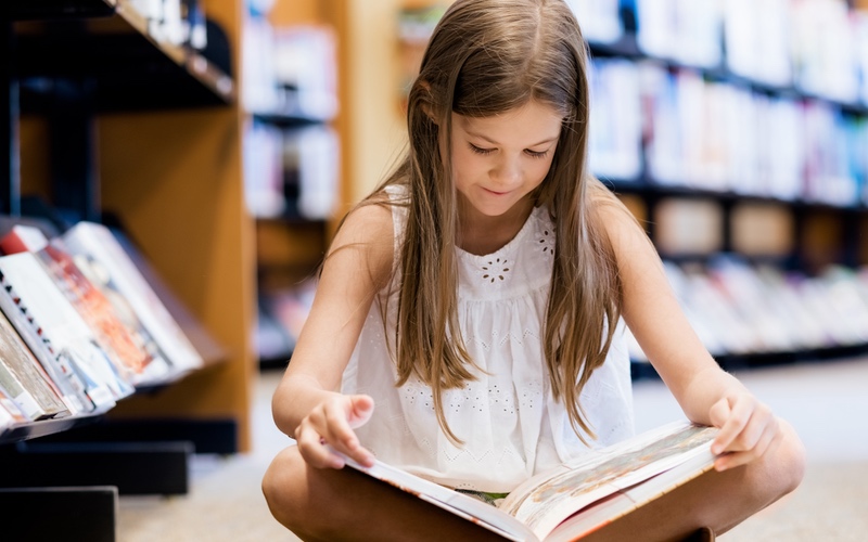 Child sitting on the floor at a library reading a book.