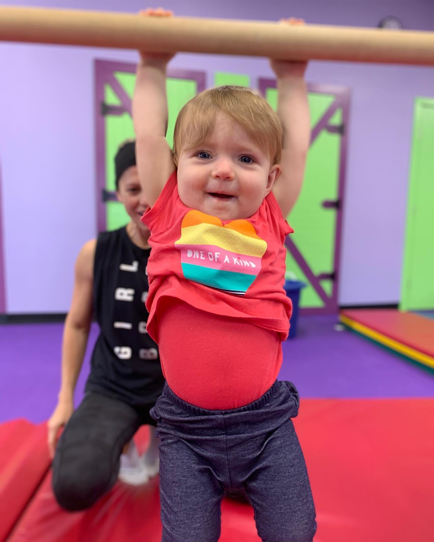 A little baby playing on blue gym equipment with a staff member. 