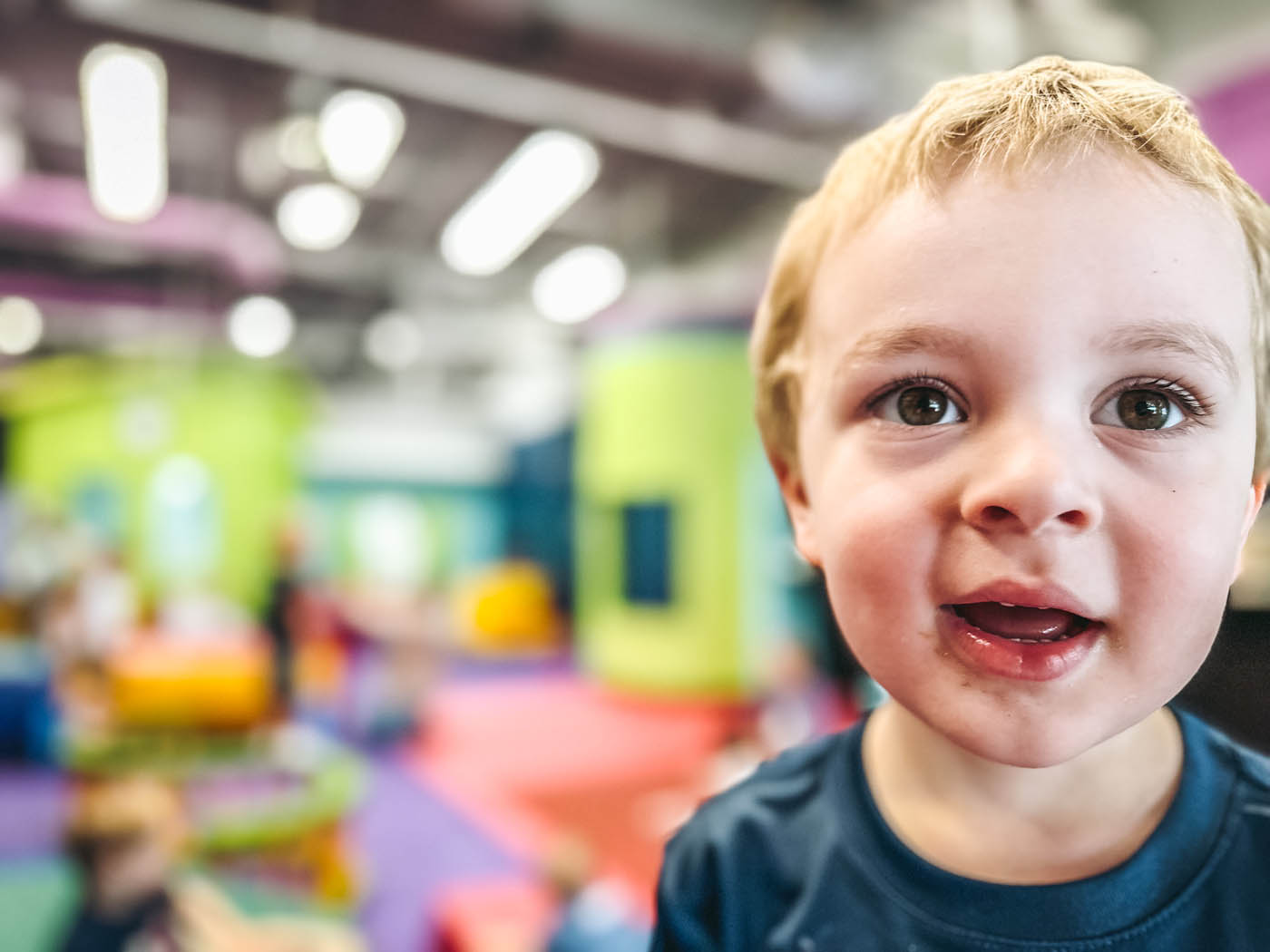 A little boy with blonde hair smiling and playing in Romp n' Roll West End's gym.