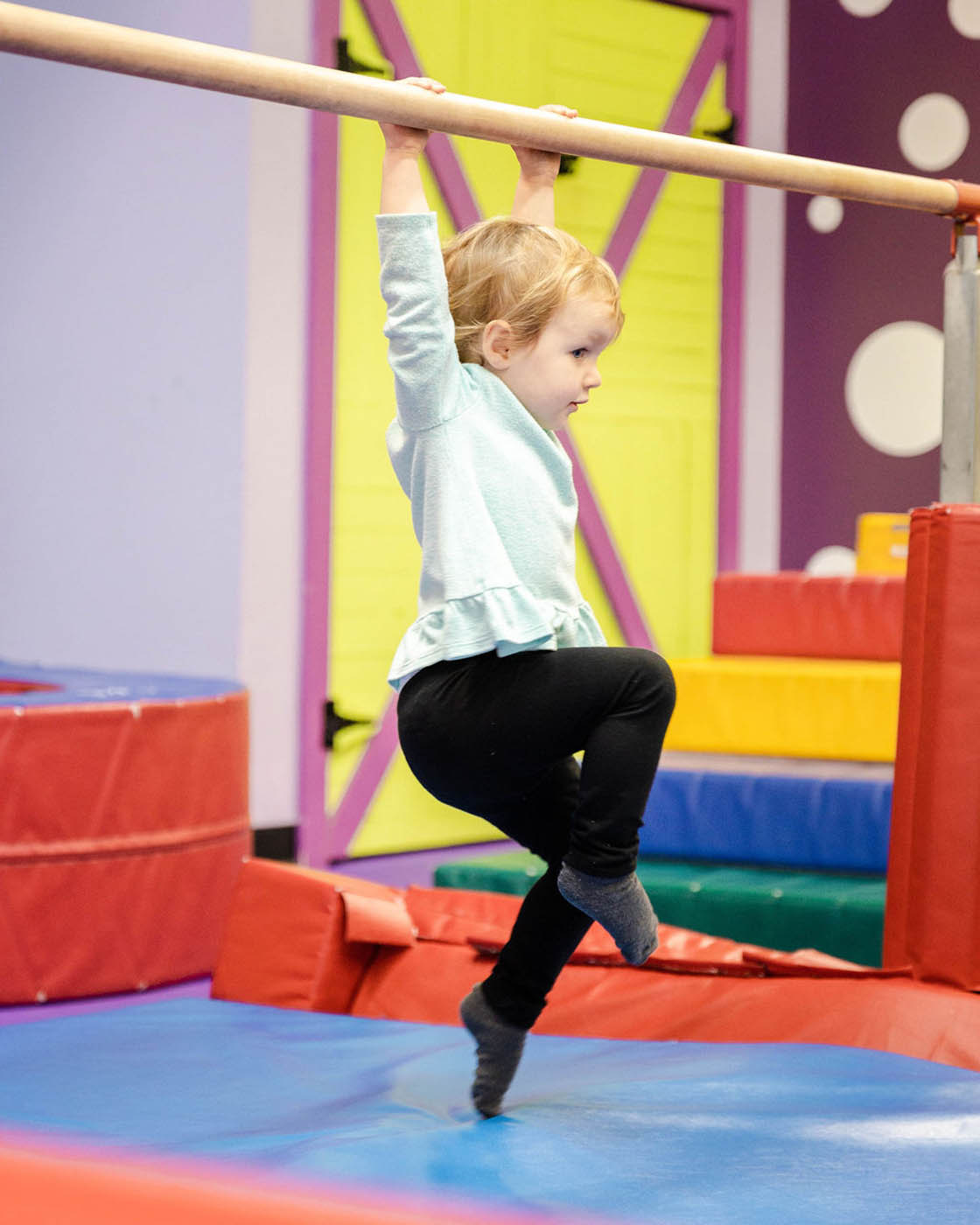 A kid swining from Romp n' Roll gym equipment - safe kids fitness classes in Katy, TX.