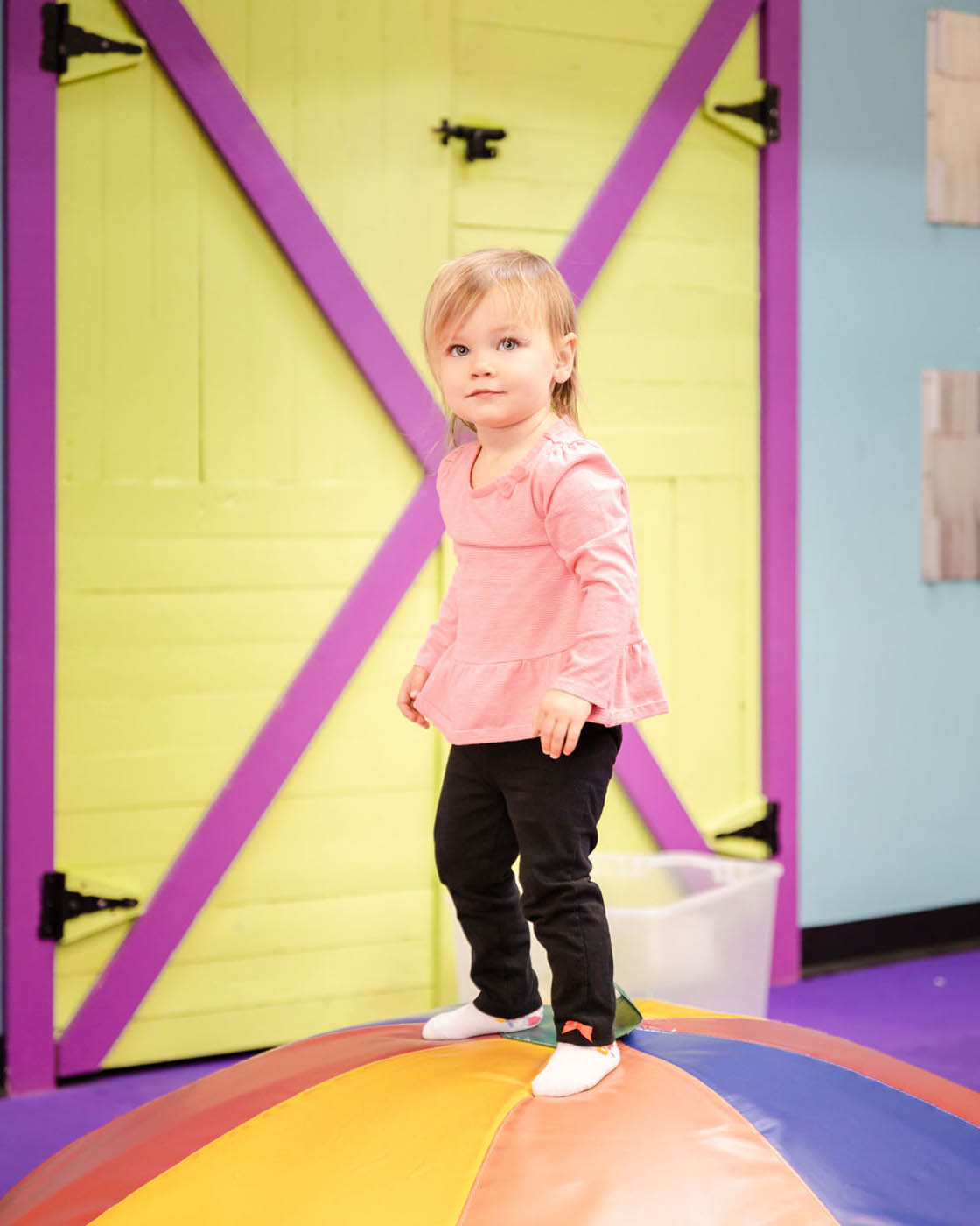 A girl standing on top of some mats used for gymnastic classes for 2 year olds in Glen Allen, VA at Romp n' Roll.