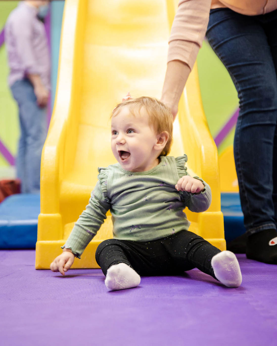 A young boy that just went down a yellow slide at Romp n' Roll.