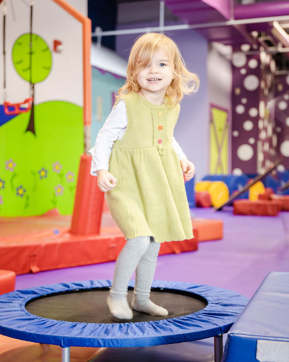 A little girl in a green dress playing on Romp n' Roll's gym equipment, contact us today for indoor kids activities in Midlothian, VA.