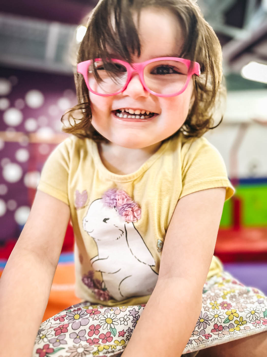 A little girl with pink glasses laughing with her peers at Romp n' Roll West End.