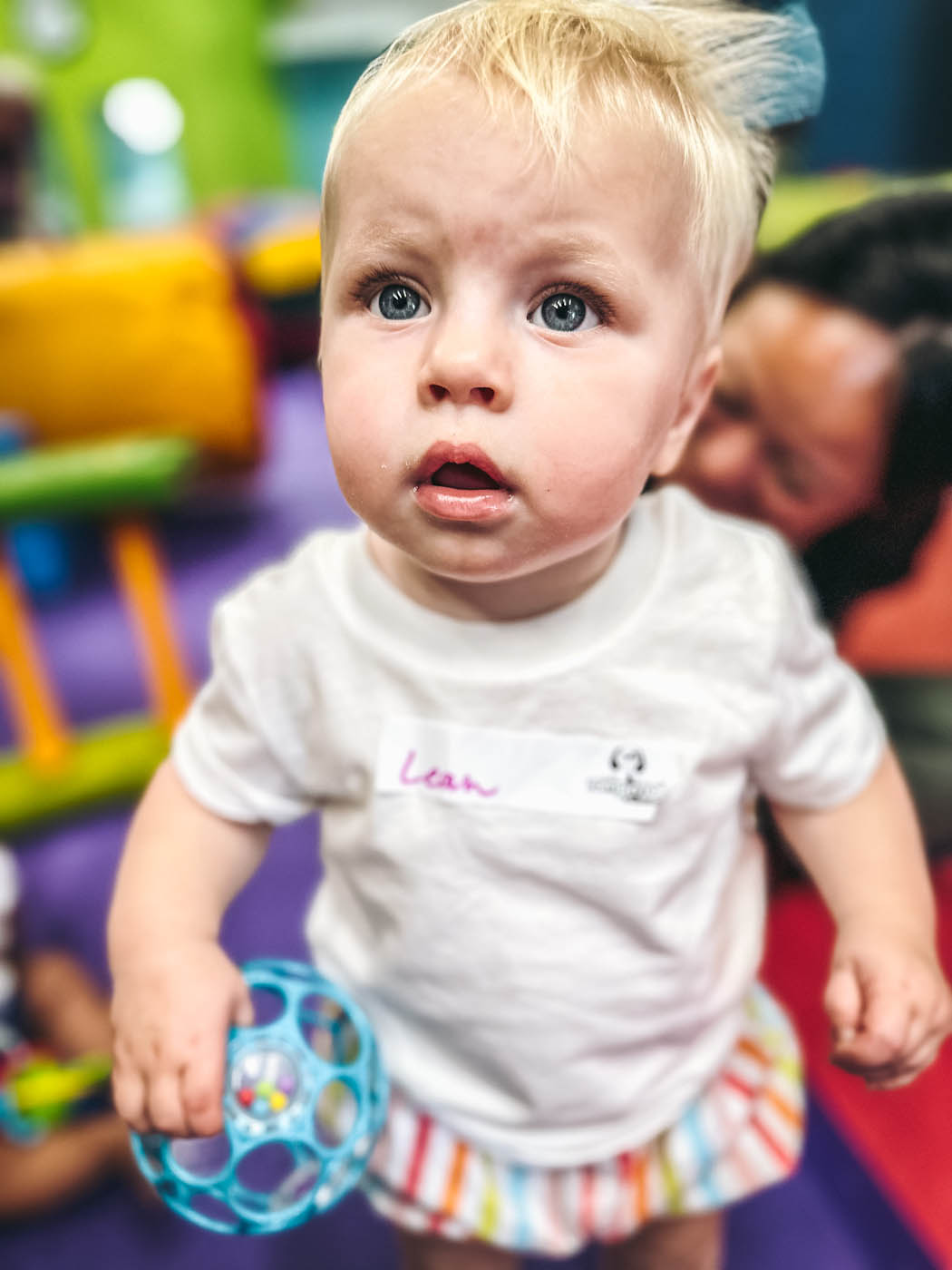 A very little boy holding a blue ball in a sports class with Romp n' Roll in Raleigh.