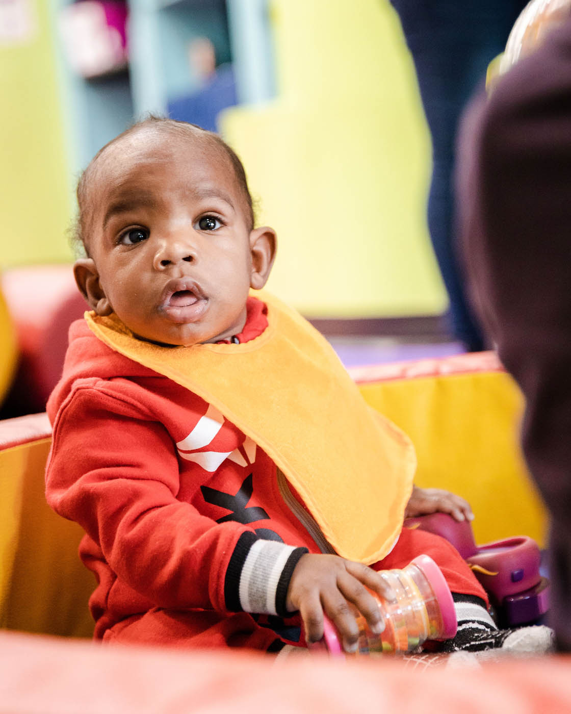 A baby with a yellow bib at a Romp n' Roll facility in Katy.