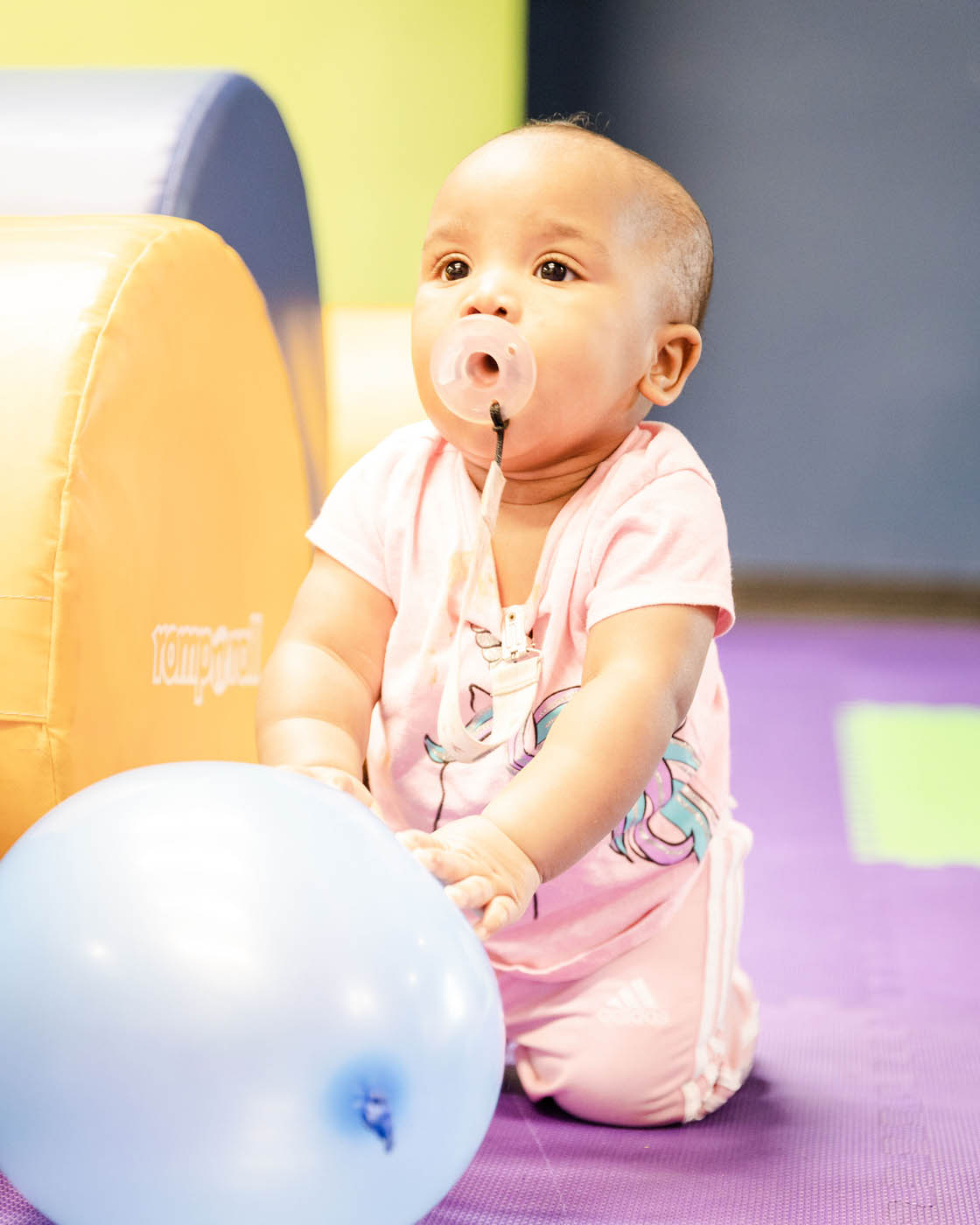 A baby in a gym class working on basic motor skills and enjoying playing with a blue ball - Romp n' Roll in Katy.