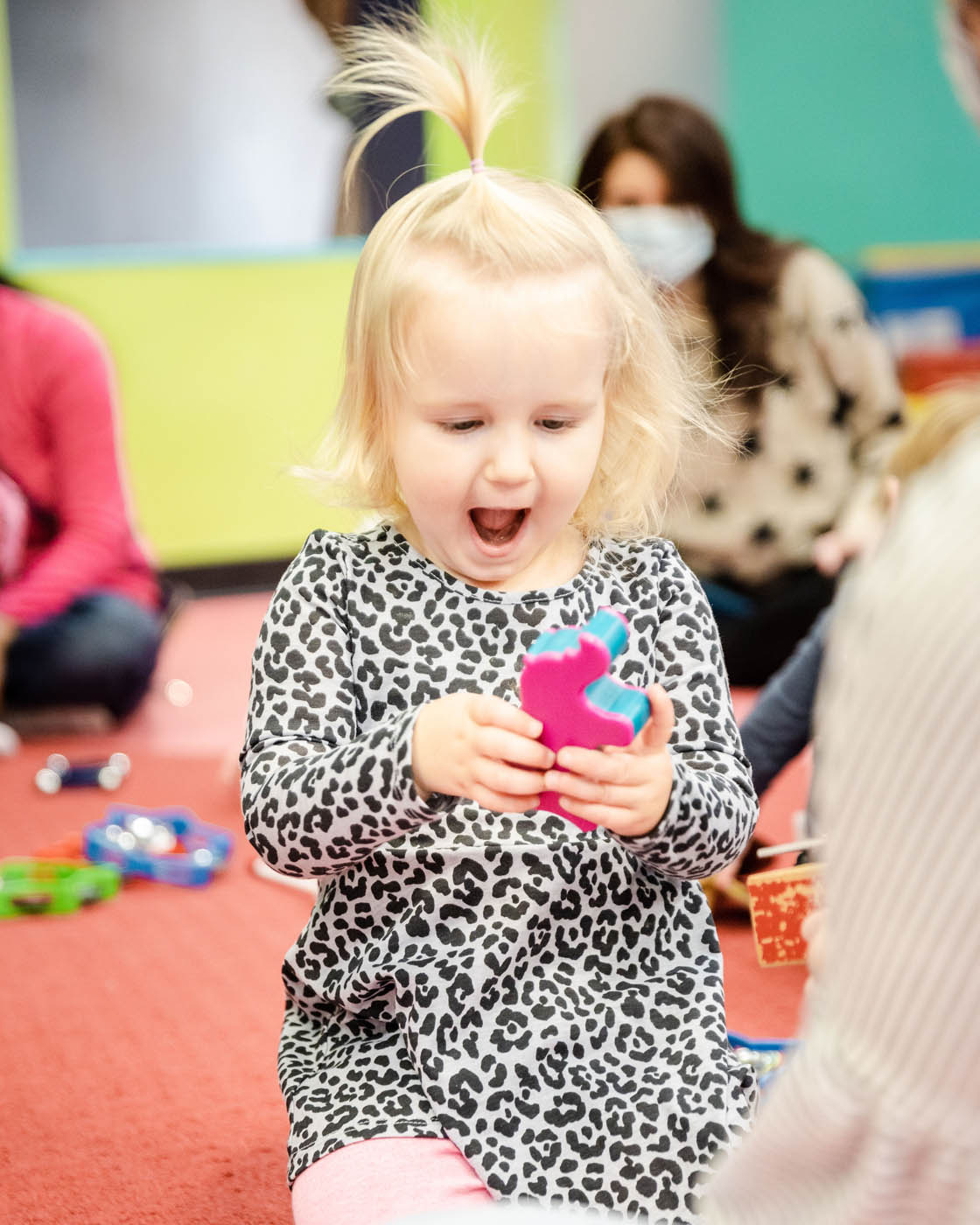 A littel girl with blonde hair holding a toy and smiling at Romp n' Roll in Midlothian.