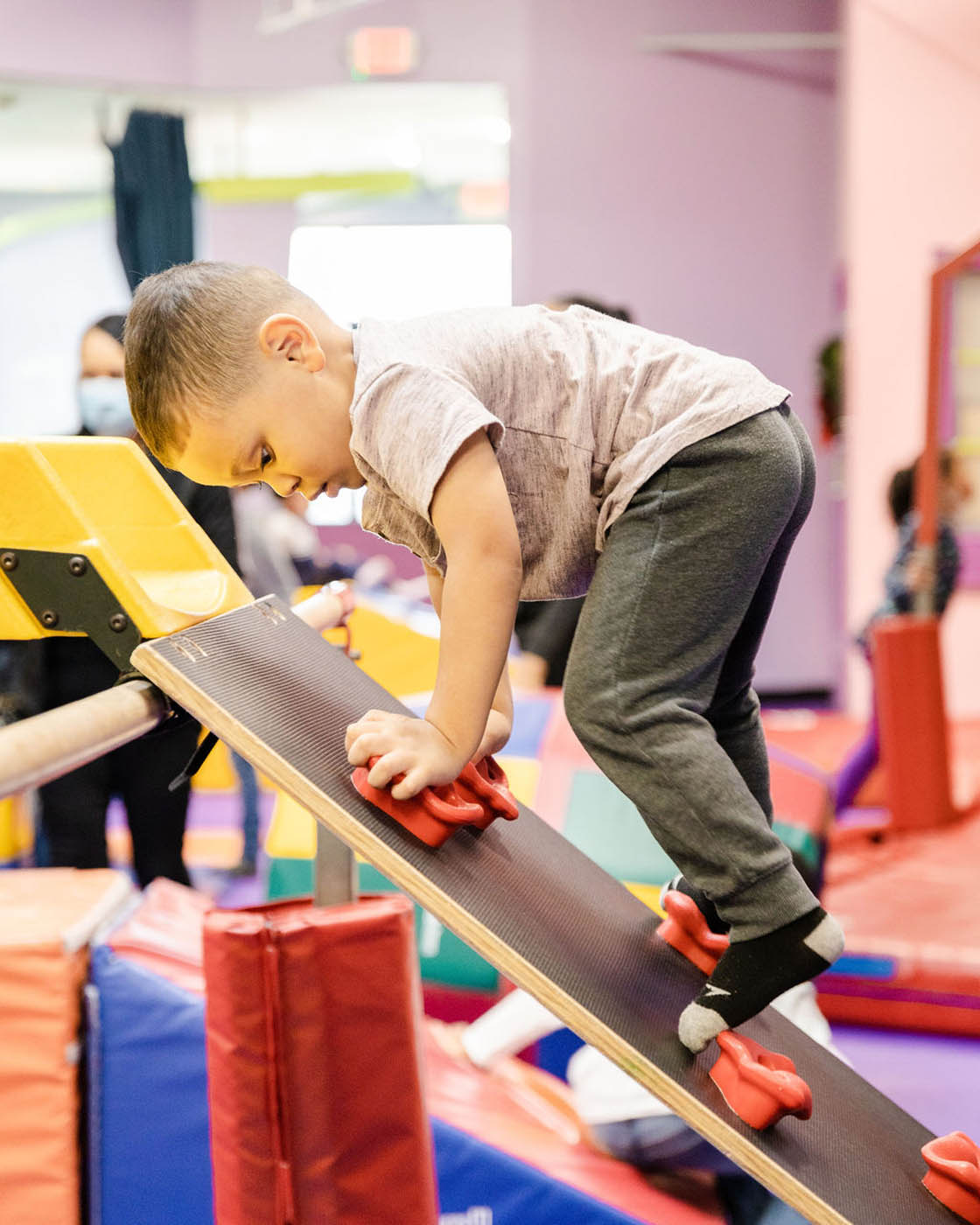 A young boy using a small climbing wall in Romp n' Roll's gym class in Katy.