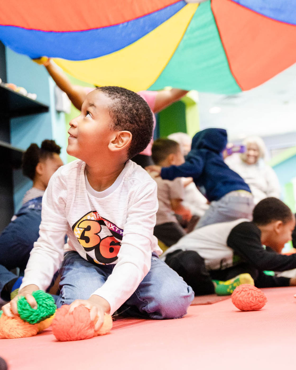 Kids playing with each other at Romp n' Roll's parachute play during mixed age classes for kids in Katy, TX.