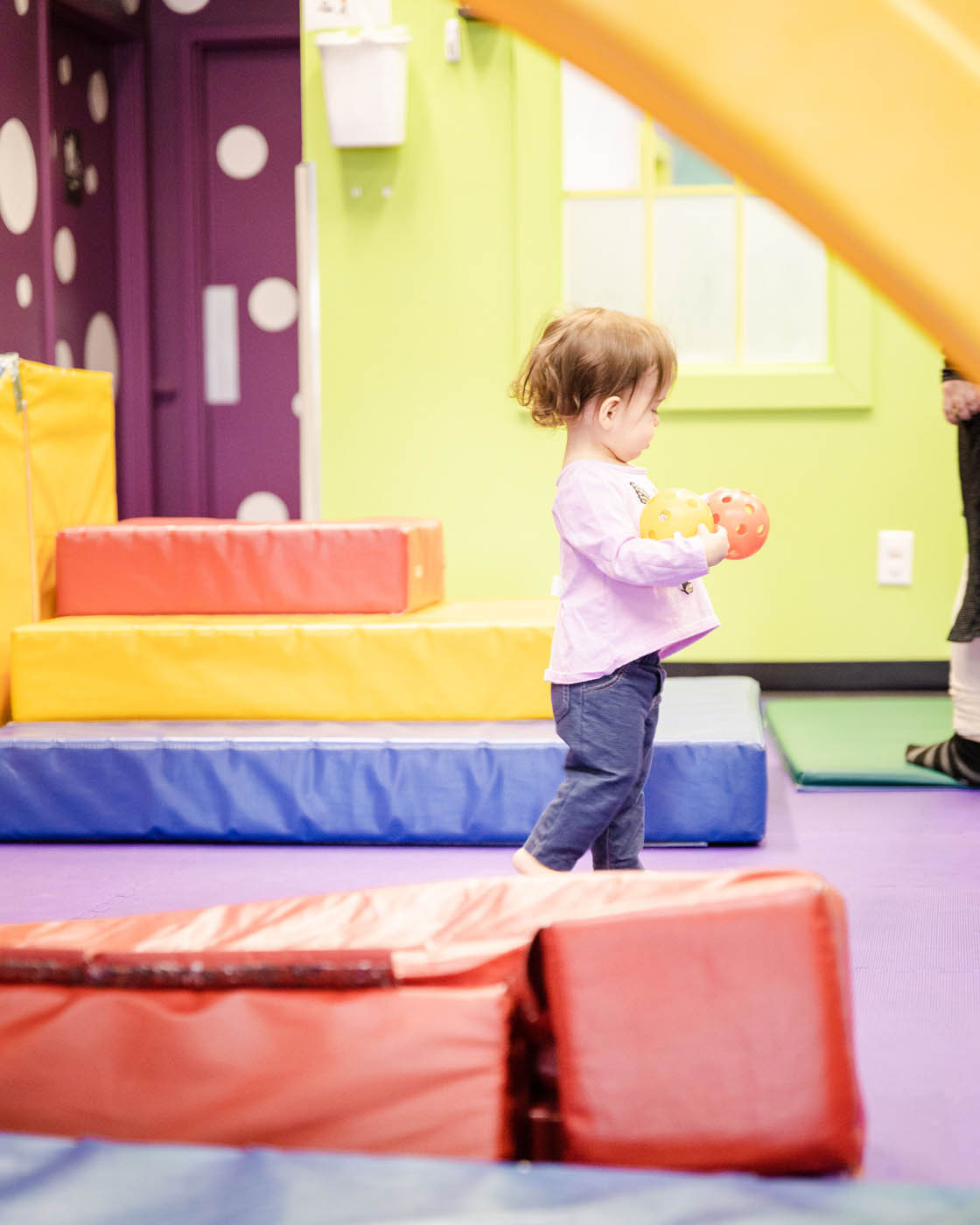 A young girl holding two balls standing at Romp n' Roll.