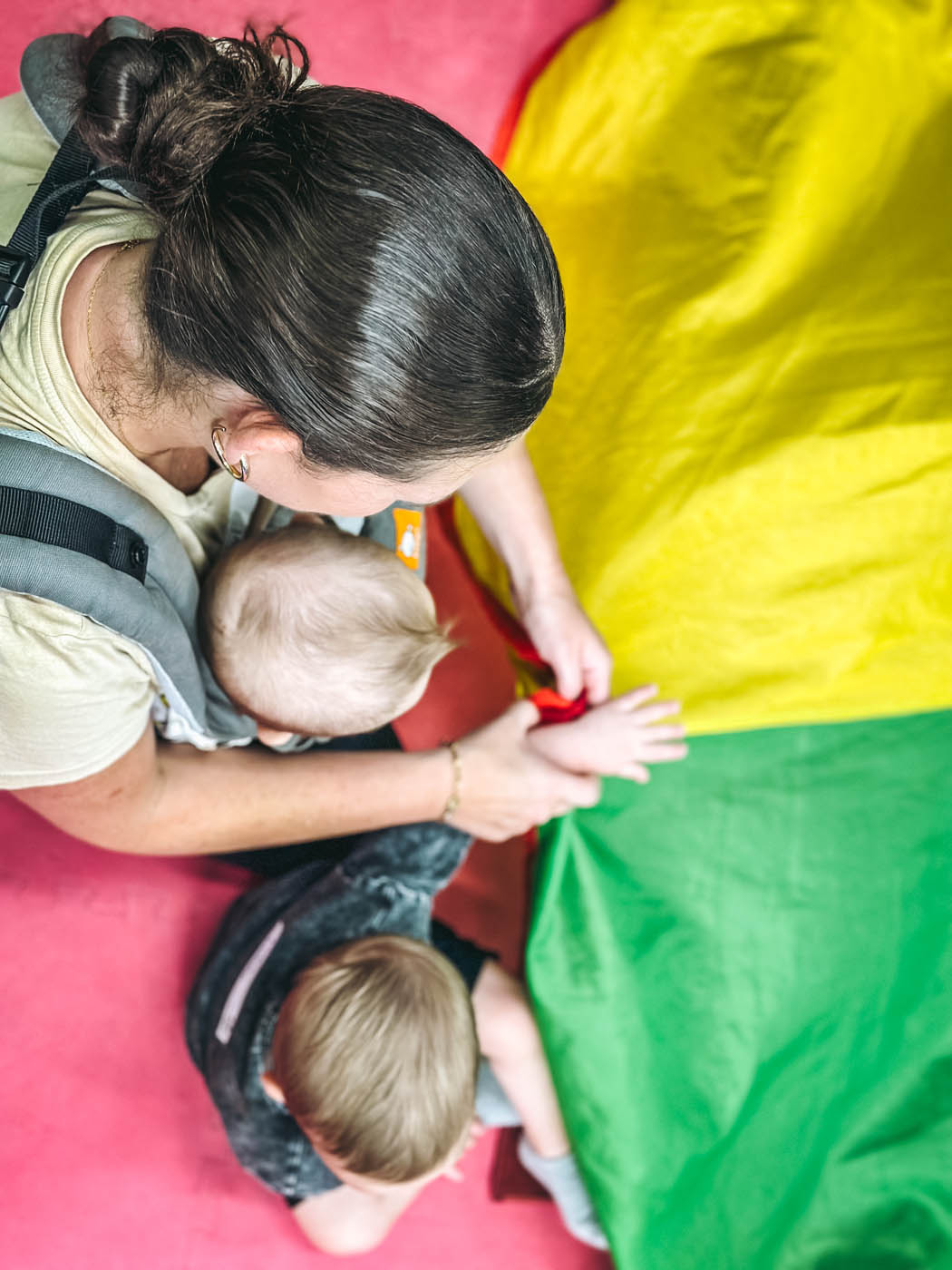 An adult with two kids playing with a colorful parachute at Romp n' Roll in Katy, TX.