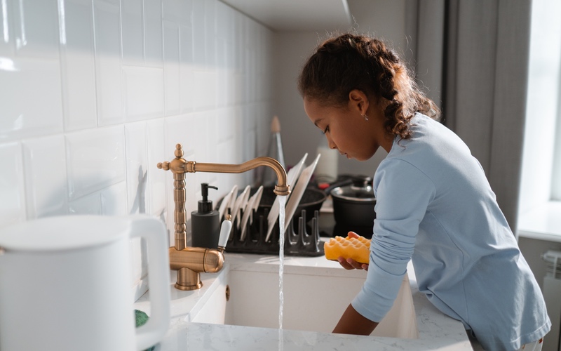 A young child standing at a kitchen sink and helping wash dishes.