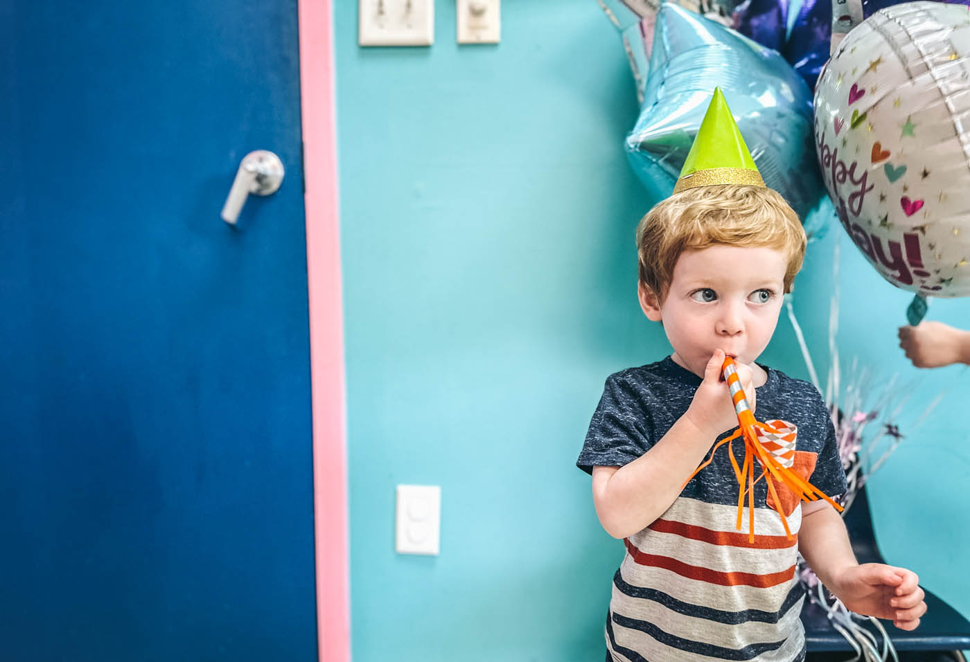 A boy with a green party hat on and birthday balloons at Romp n' Roll in Glen Allen, VA.