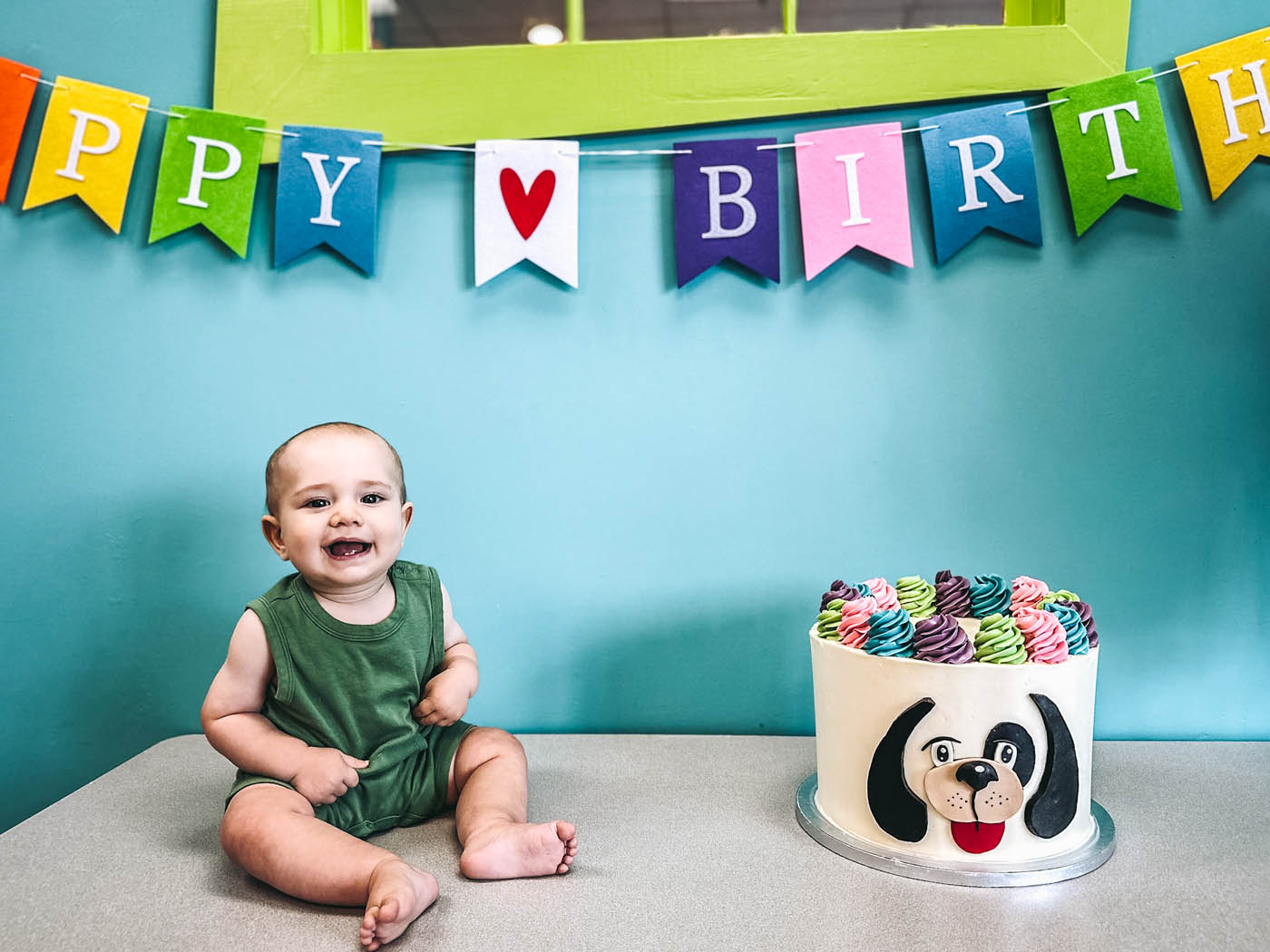 A baby sitting on a table with a Romp n' Roll Rompy cake - a place for birthday party business opportunities.